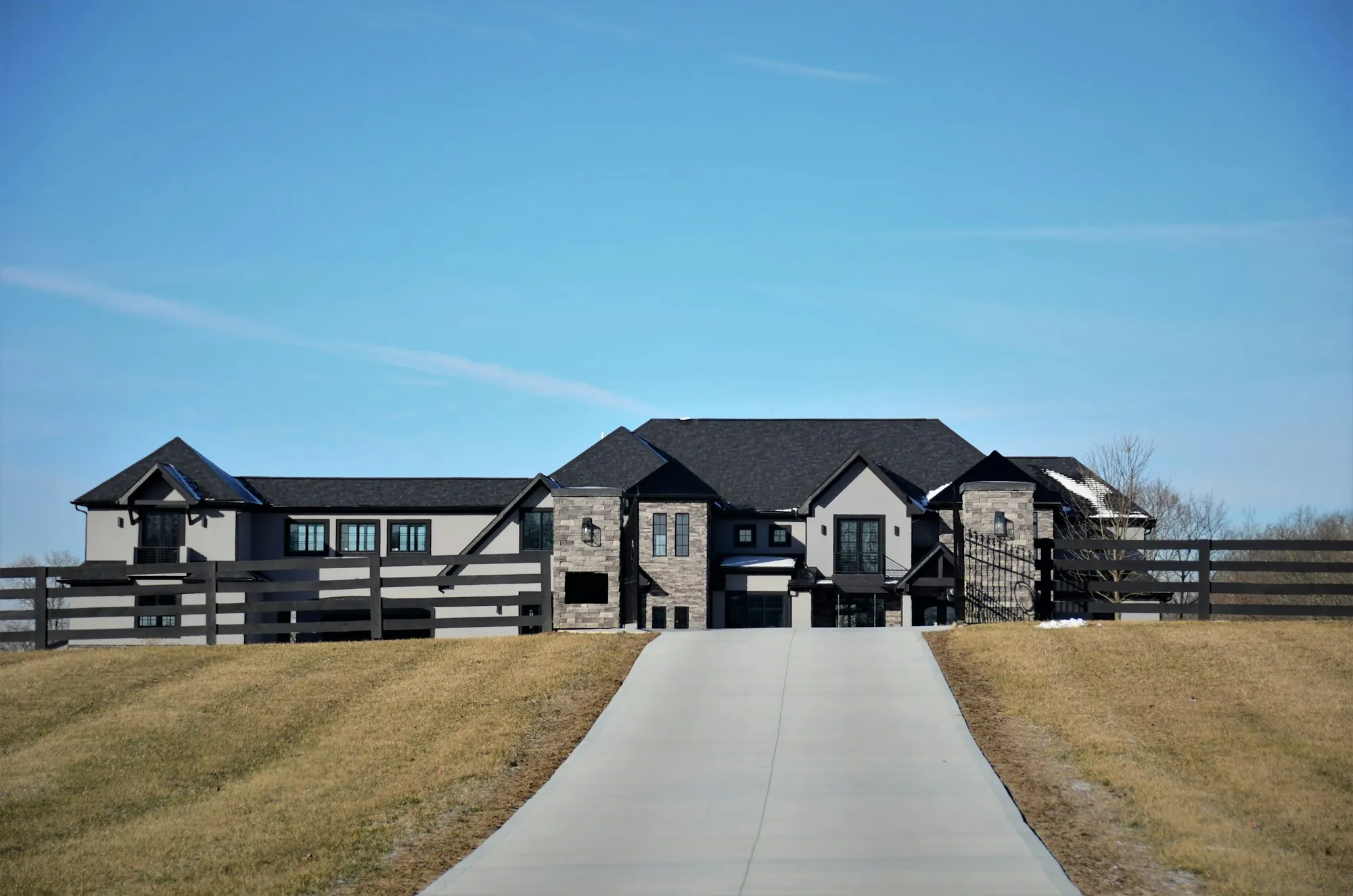 Dark stone home with a steep black roof at the end of a long driveway