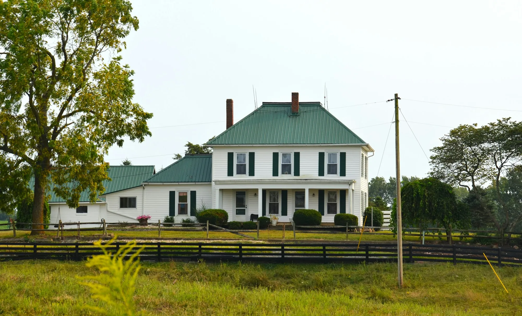 White farmhouse with a green metal roof behind a fence