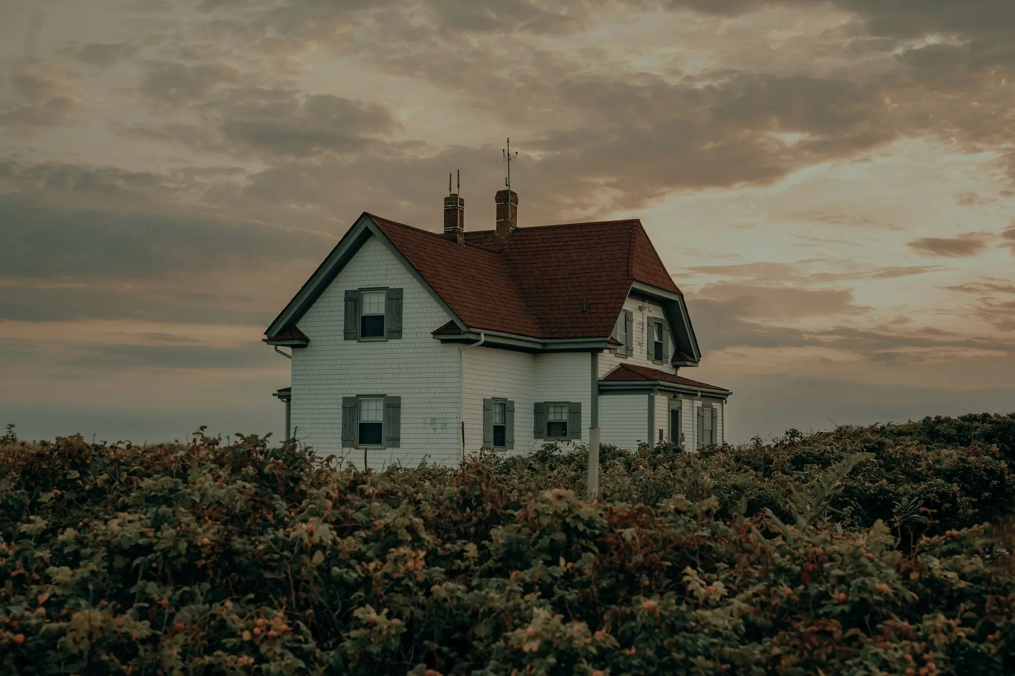 White farmhouse with a red shingle roof and twin chimneys at sunset