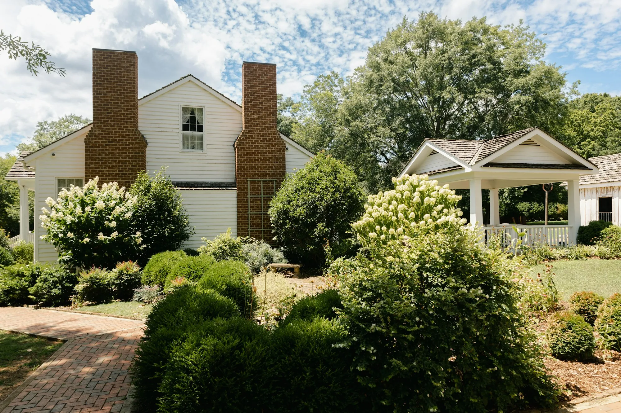 White colonial home with a brick chimney behind a lush garden